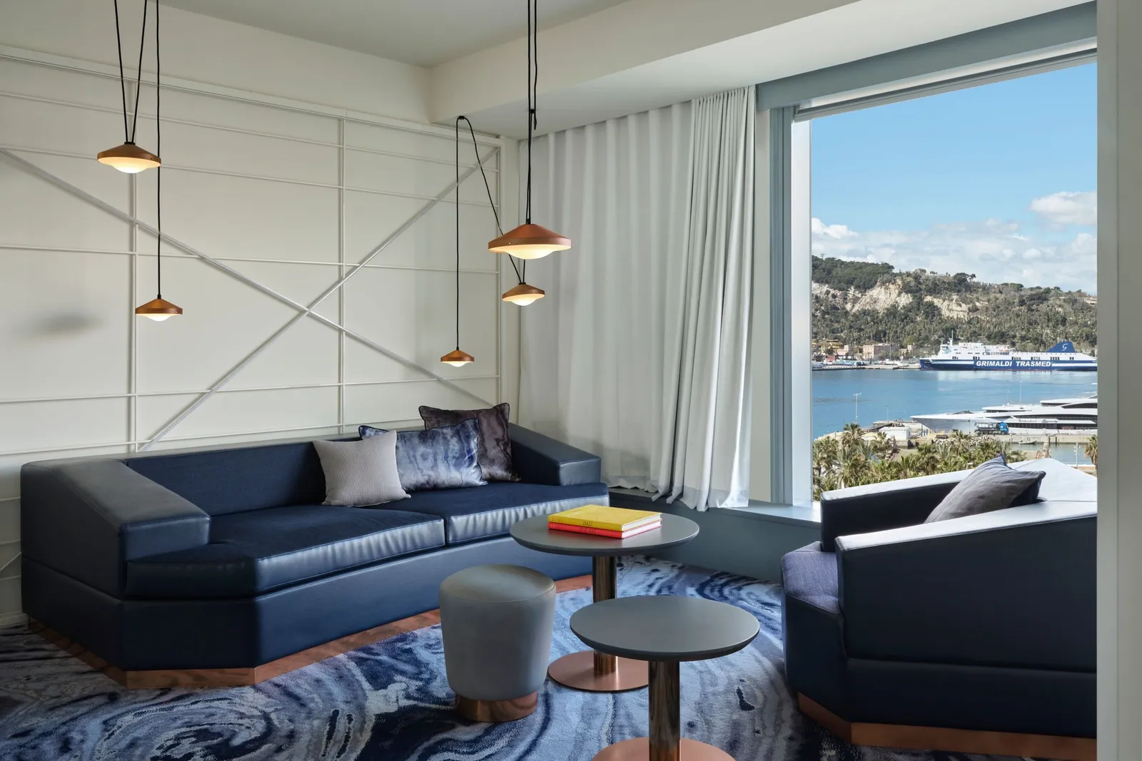 A sitting room with a navy sofa, pendant lamps and the port and its ferries through the window