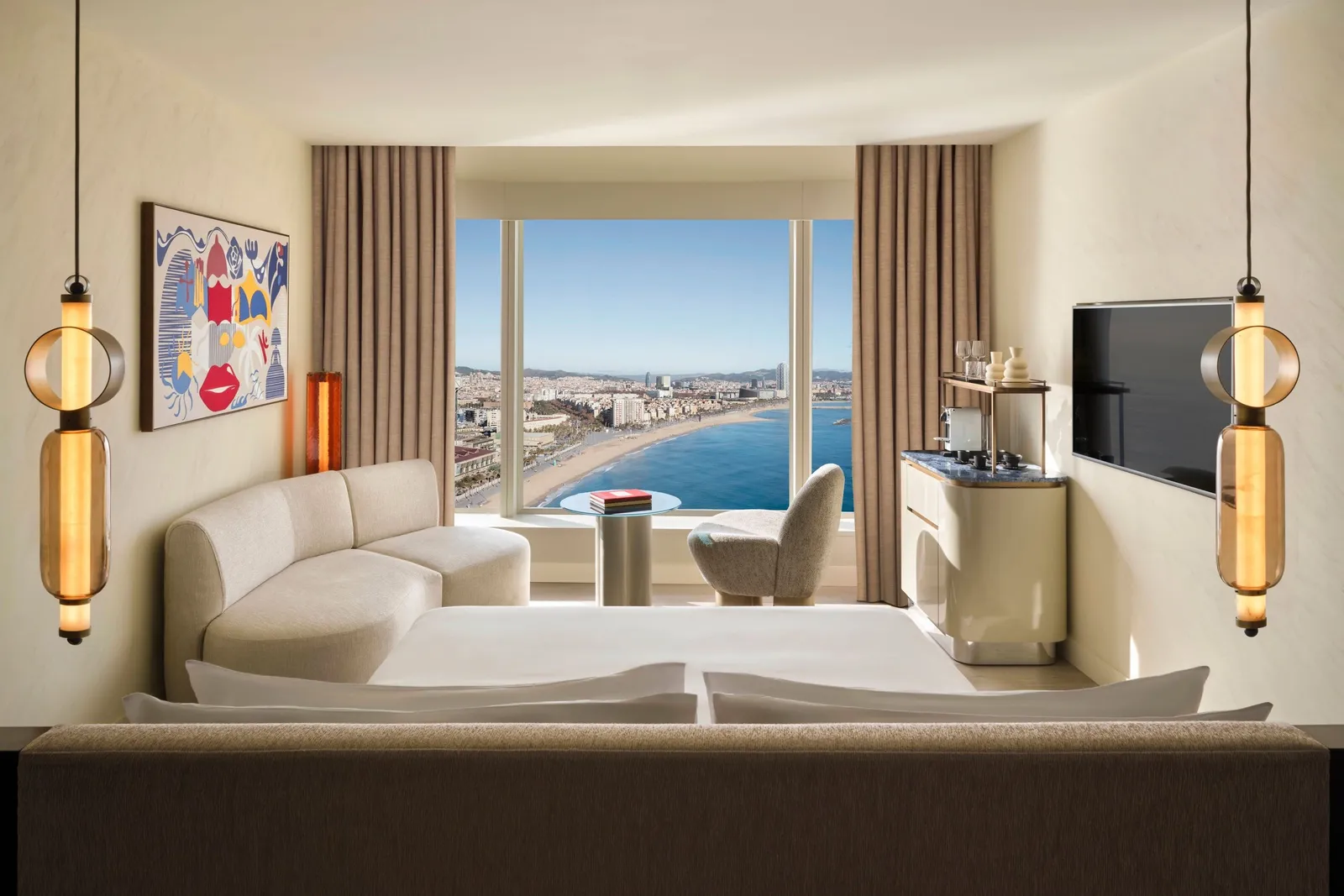 A room with a white sofa and Barceloneta beach beyond the window