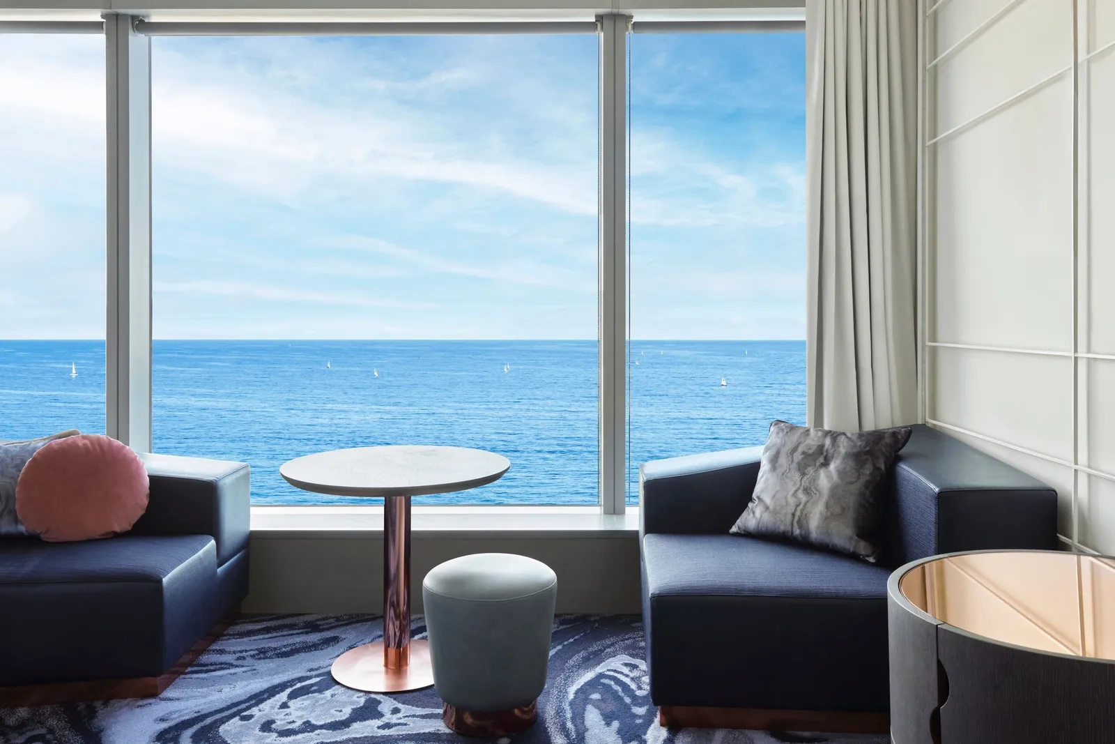 2 navy armchairs and a small table at a window on the open sea