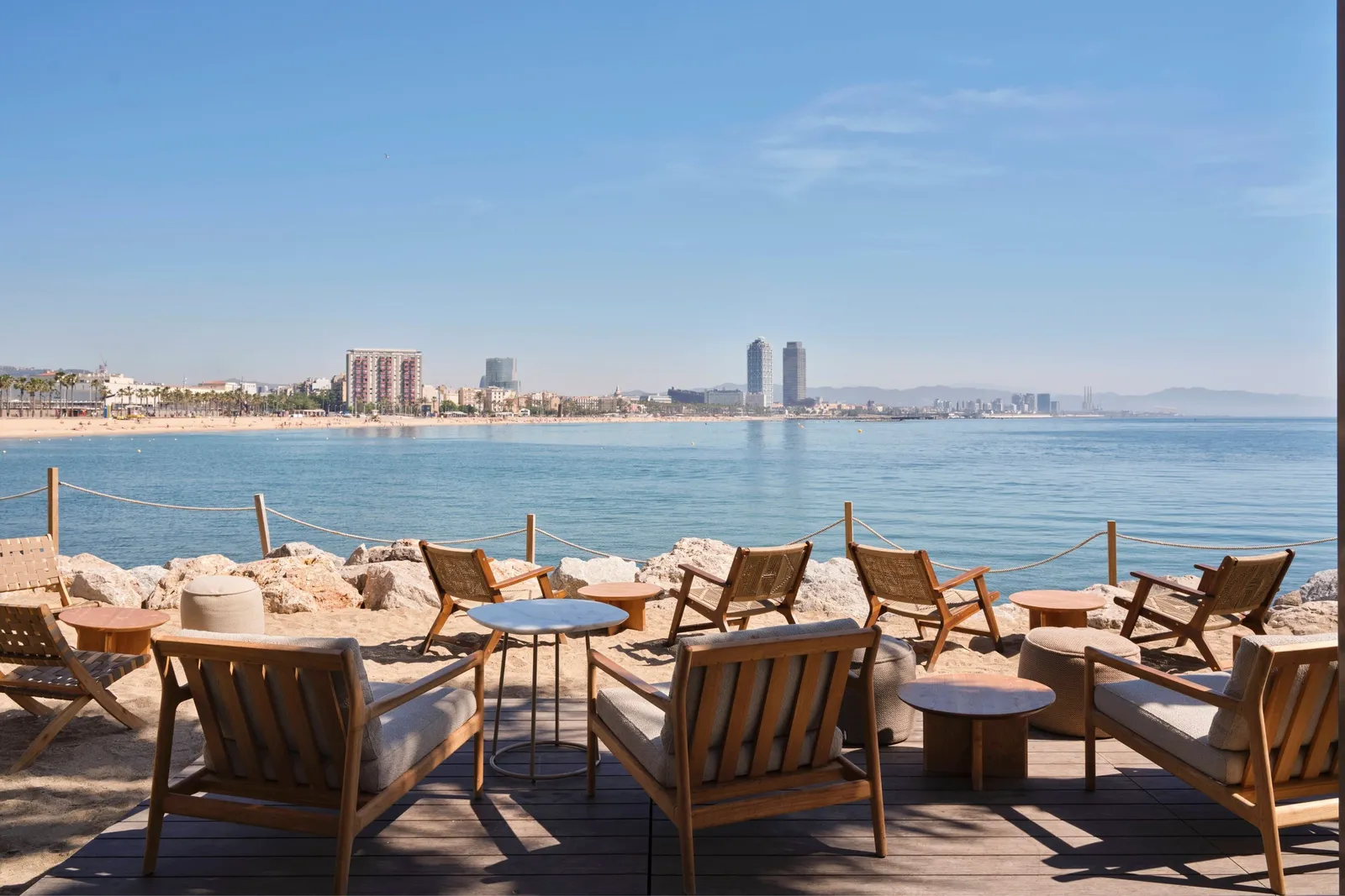 SALT’s timber armchairs on the rocks, with the beach and the Port Olímpic towers