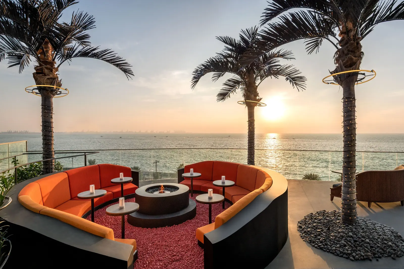 SoBe’s terrace at sunset, with orange sofas around the fire and palms
