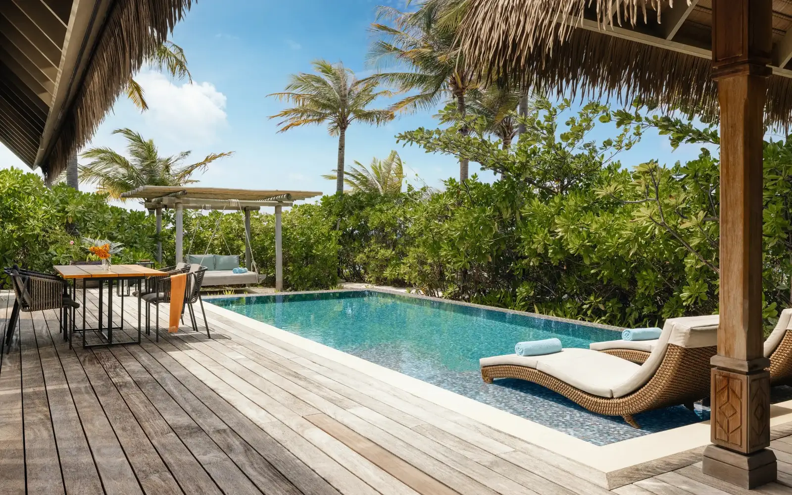 A beach villa’s deck, its pool and loungers among the greenery