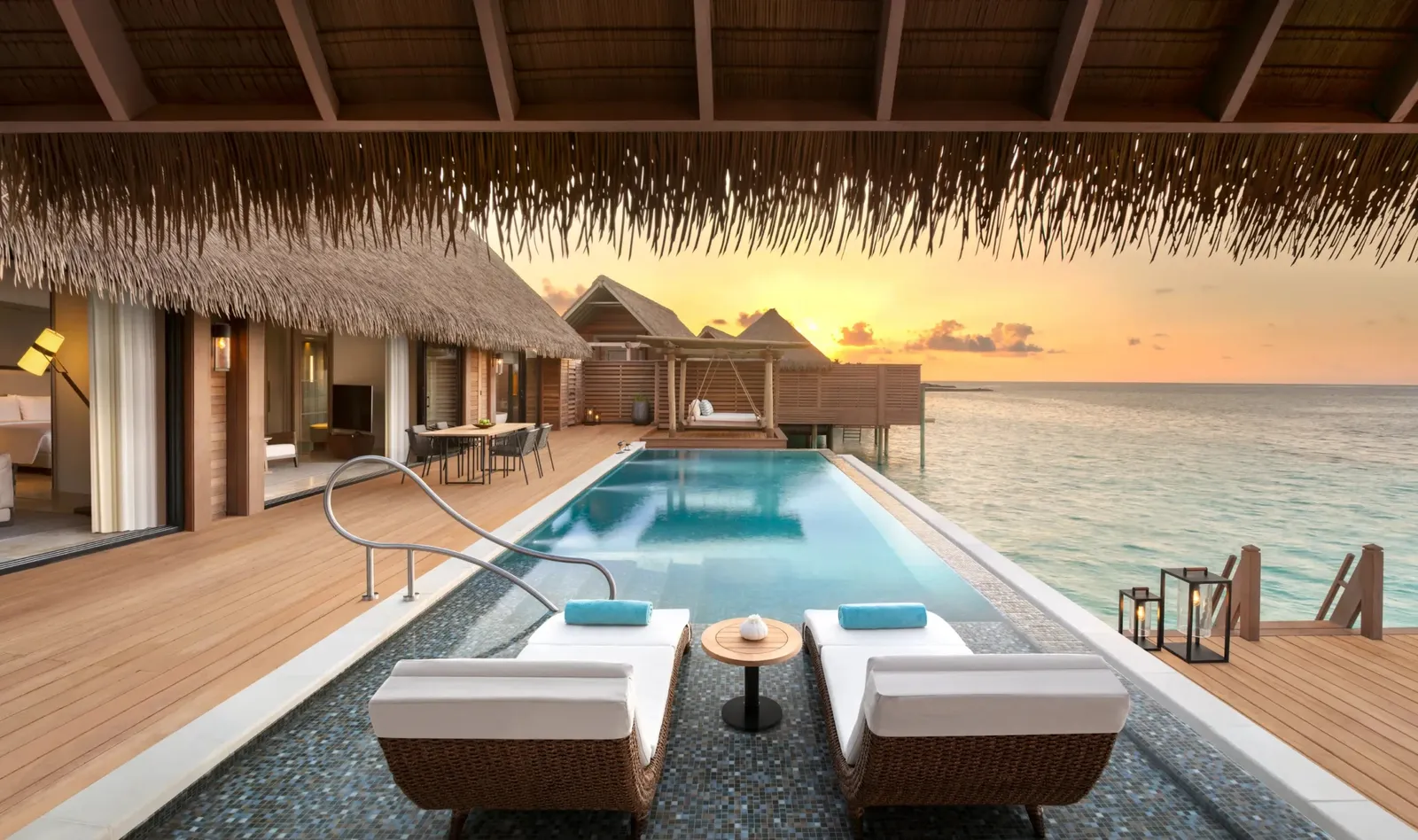 An overwater villa’s infinity pool at sunset, loungers on the deck