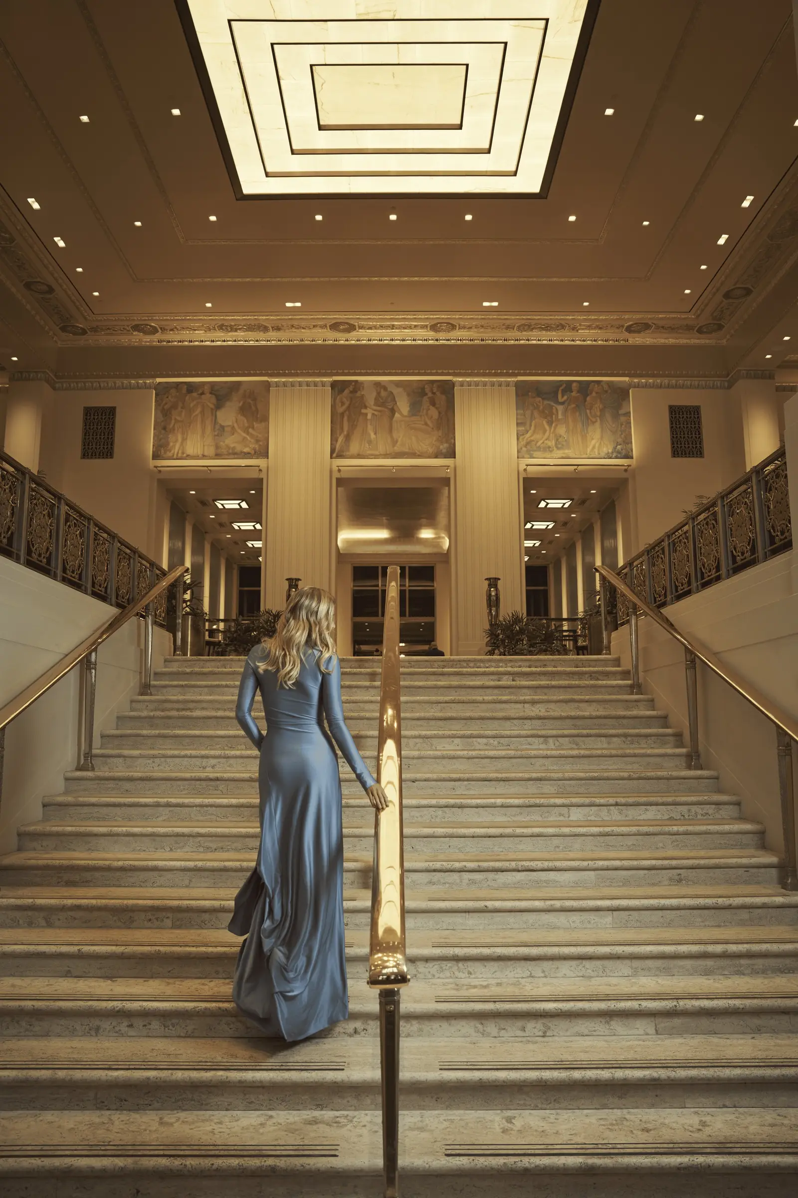 The marble stair from the Park Avenue lobby, a guest in blue climbing under the murals