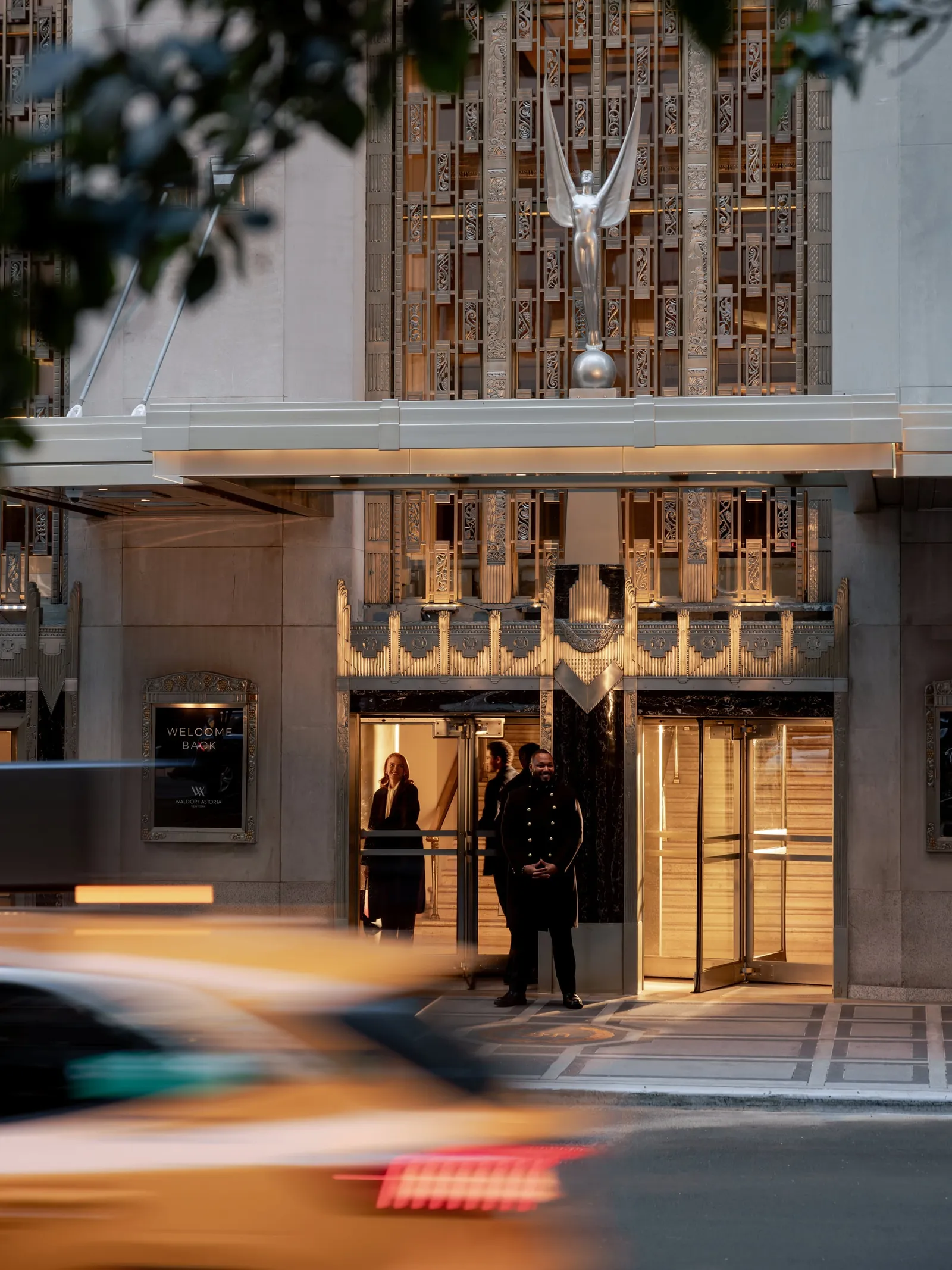 The Park Avenue entrance at dusk, a doorman and a guest under the Art Deco grille