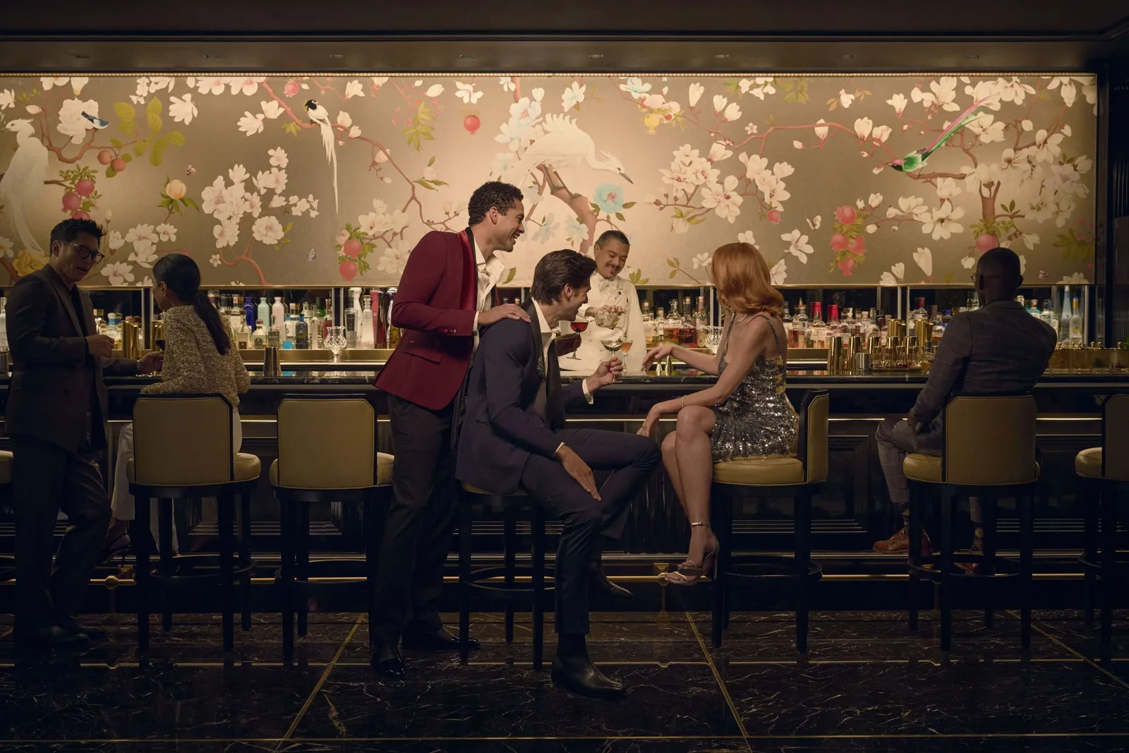Guests at the Peacock Alley bar under its painted panel, a bartender serving