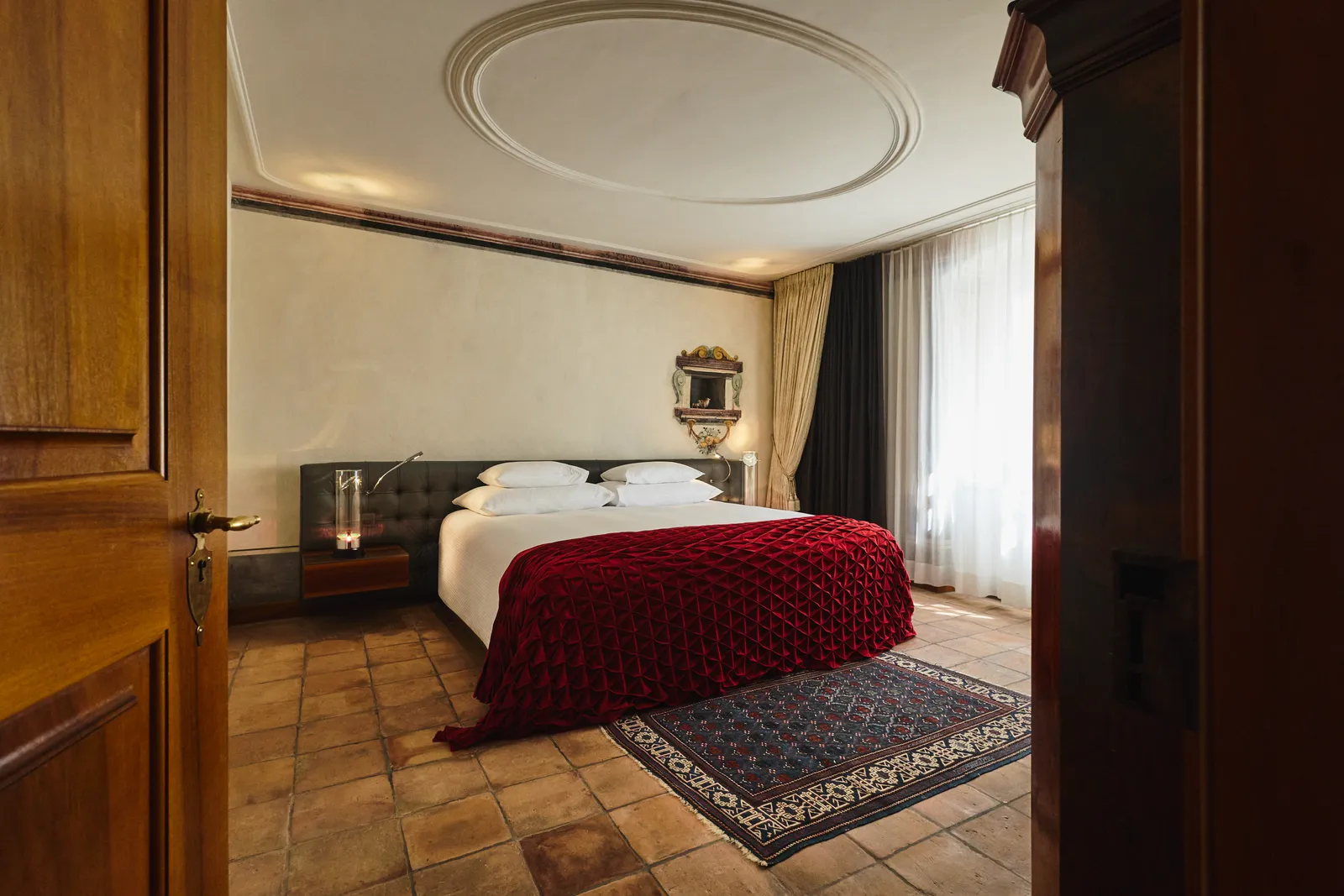 Letto con coperta rossa, parquet e soffitto bianco della suite storica