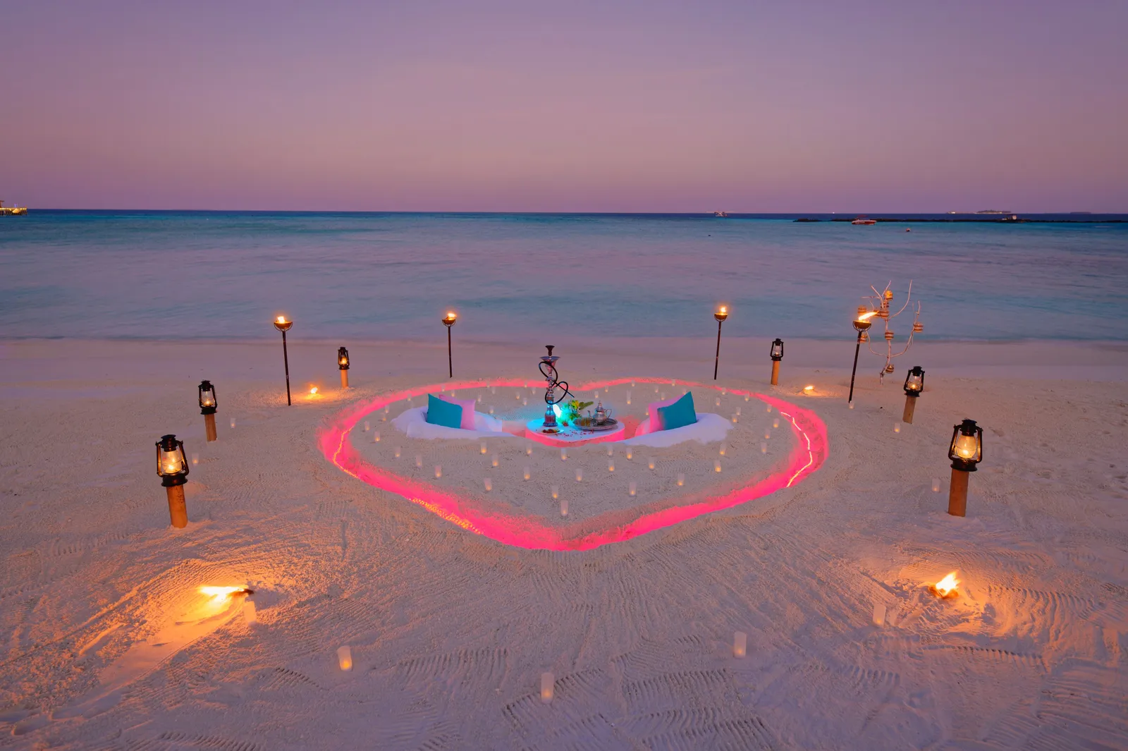 A beach dinner at dusk inside a heart of lights, among torches