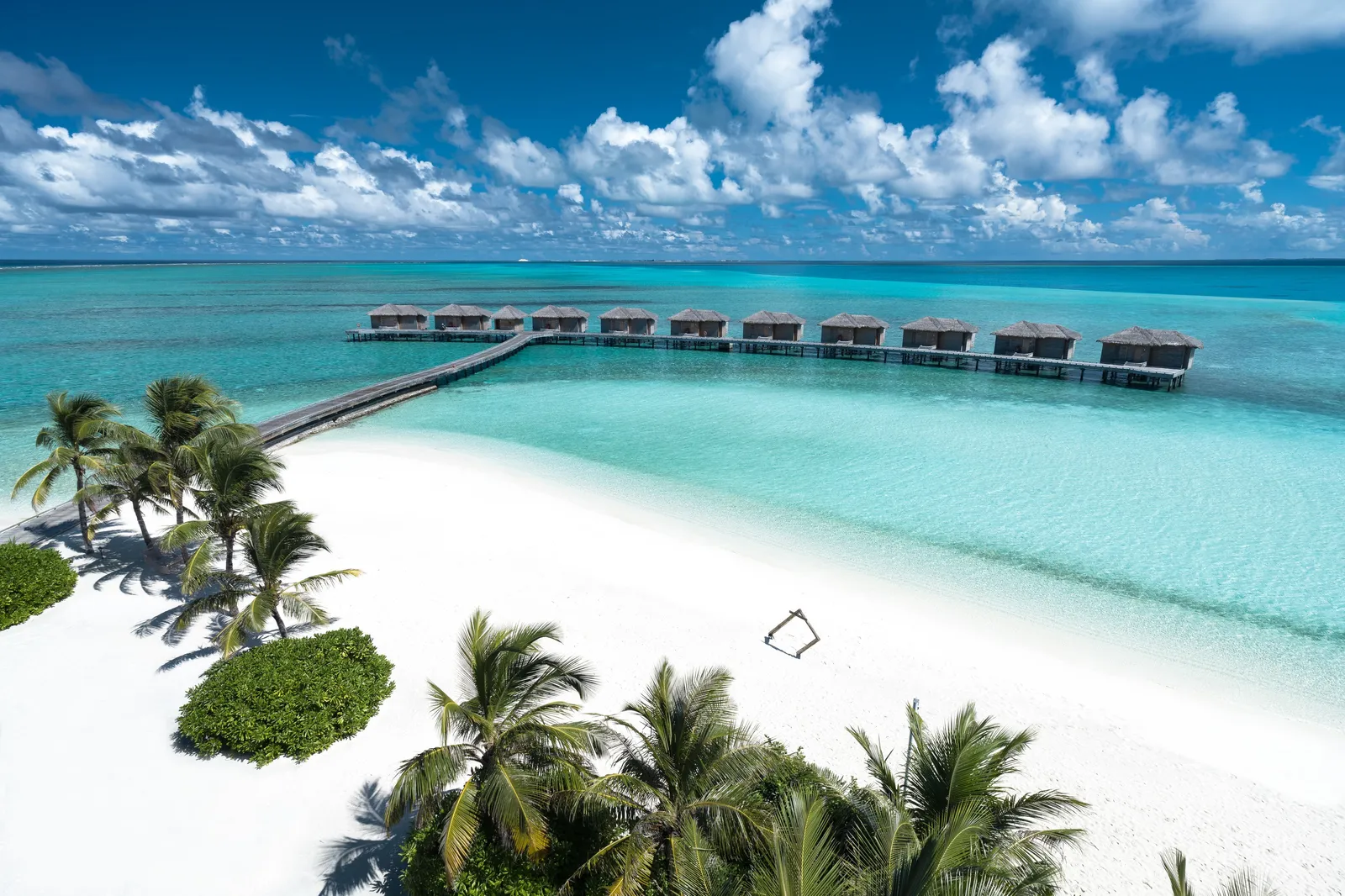 The white beach among palms and the jetty out to the row of water villas