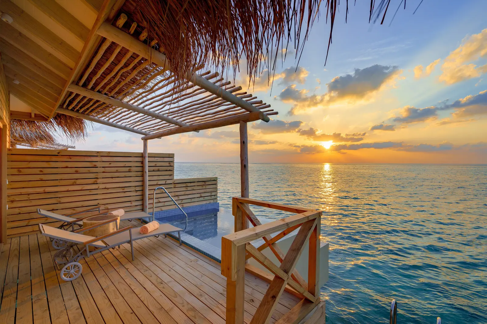A Lagoon Suite with Private Pool’s deck at sunset, its pool and a lounger above the sea