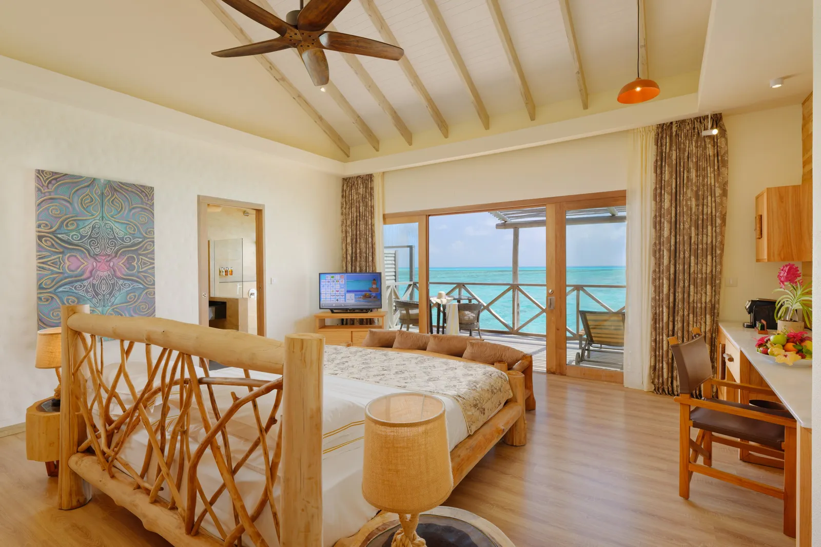 A Lagoon Villa bedroom: the bed framed in woven branches and the glass doors to the deck