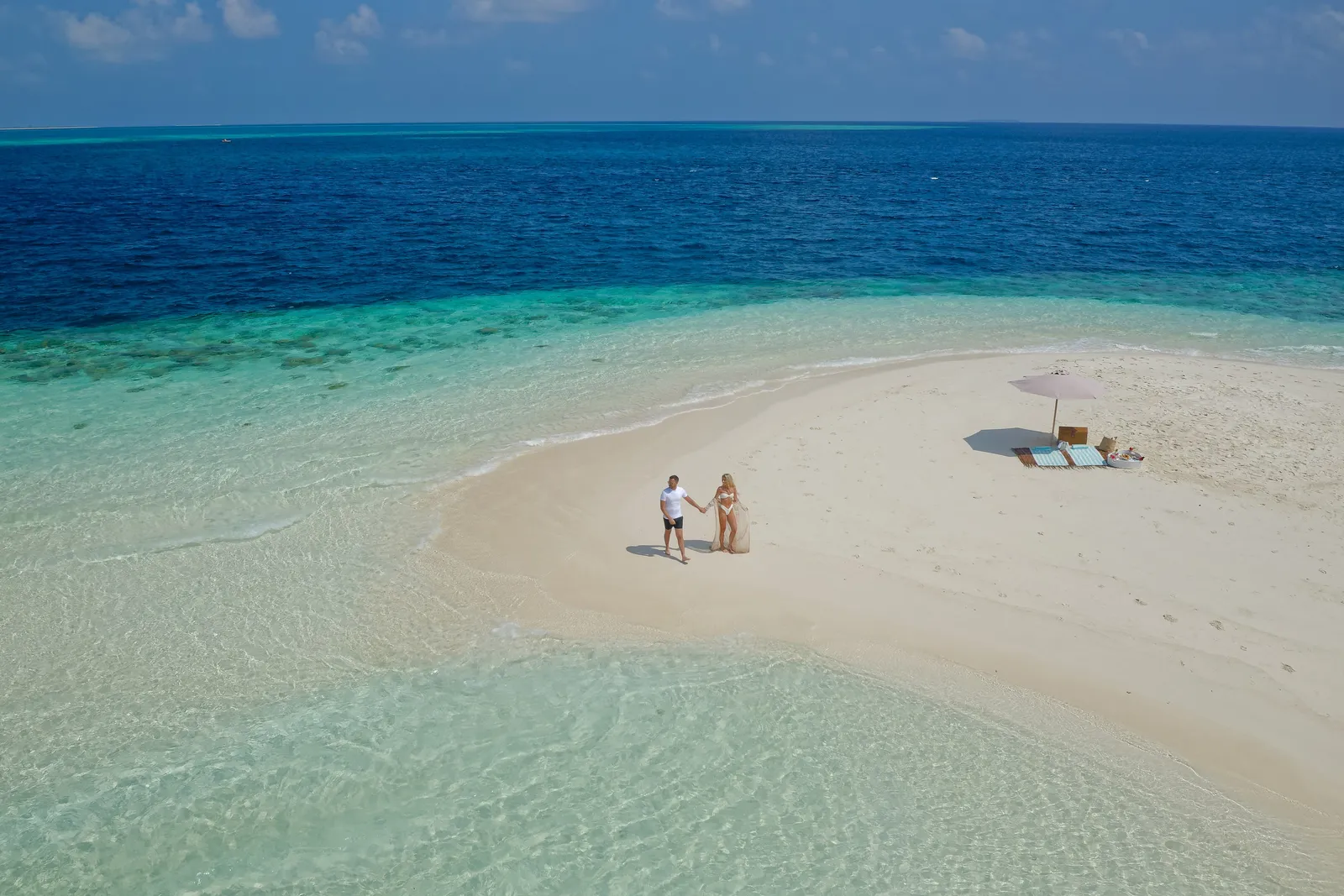 A couple on a sandbank, a parasol and cushions laid out for a picnic