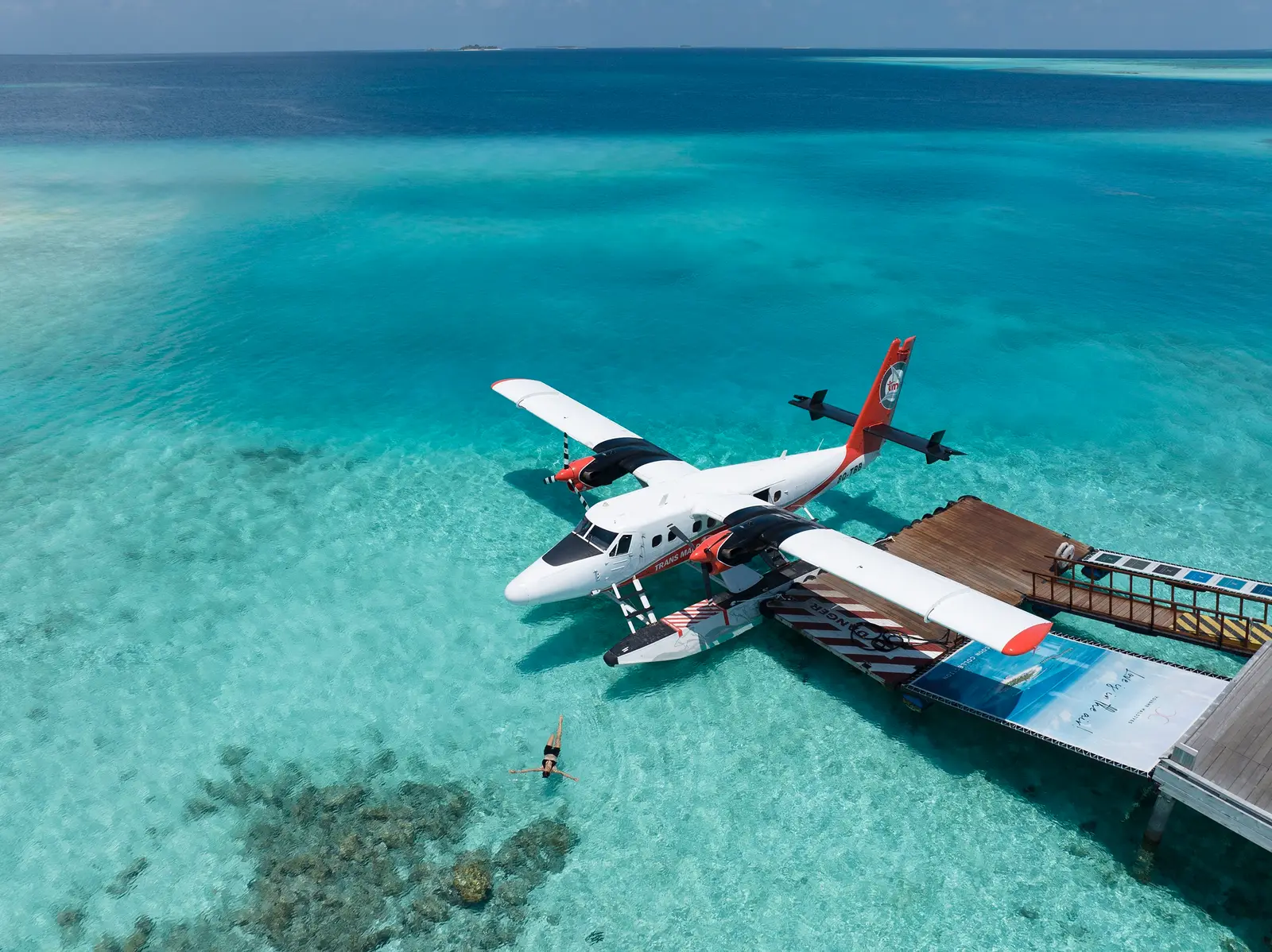 A seaplane moored at the platform in the lagoon, a swimmer beside it