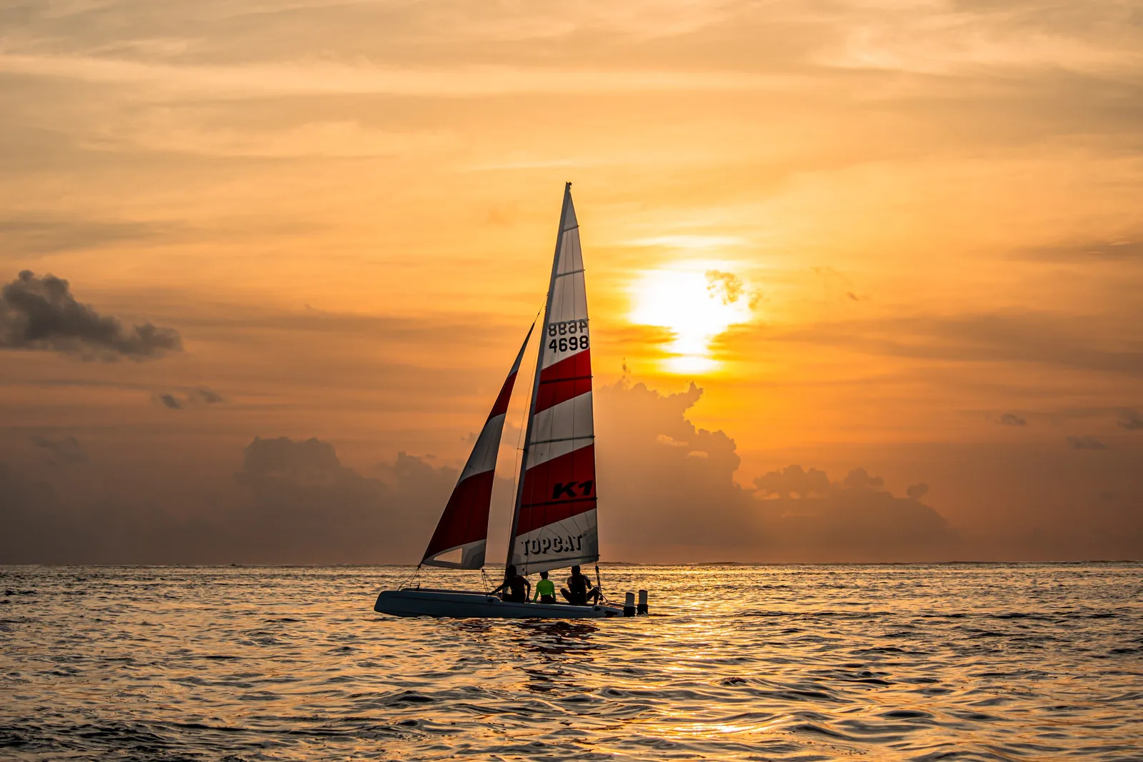 A sailing catamaran at sunset, the sun low over the sea