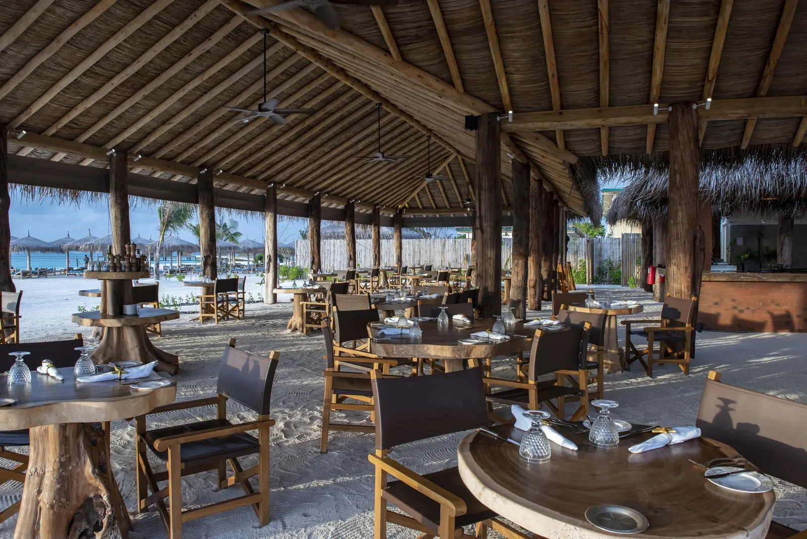The Sand’s dining room under its thatched roof, wooden tables on the sand and the sea beyond
