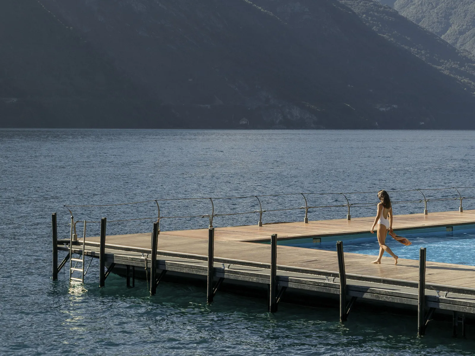 A guest walking along the floating-pool boardwalk beside Lake Como